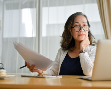 woman with papers at desk looking at laptop